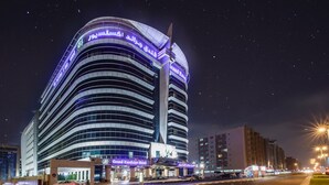 Un hôtel moderne à la façade incurvée et doté d’un éclairage décoratif, notamment d’une enseigne bien visible indiquant « Grand Excelsior Hotel ».