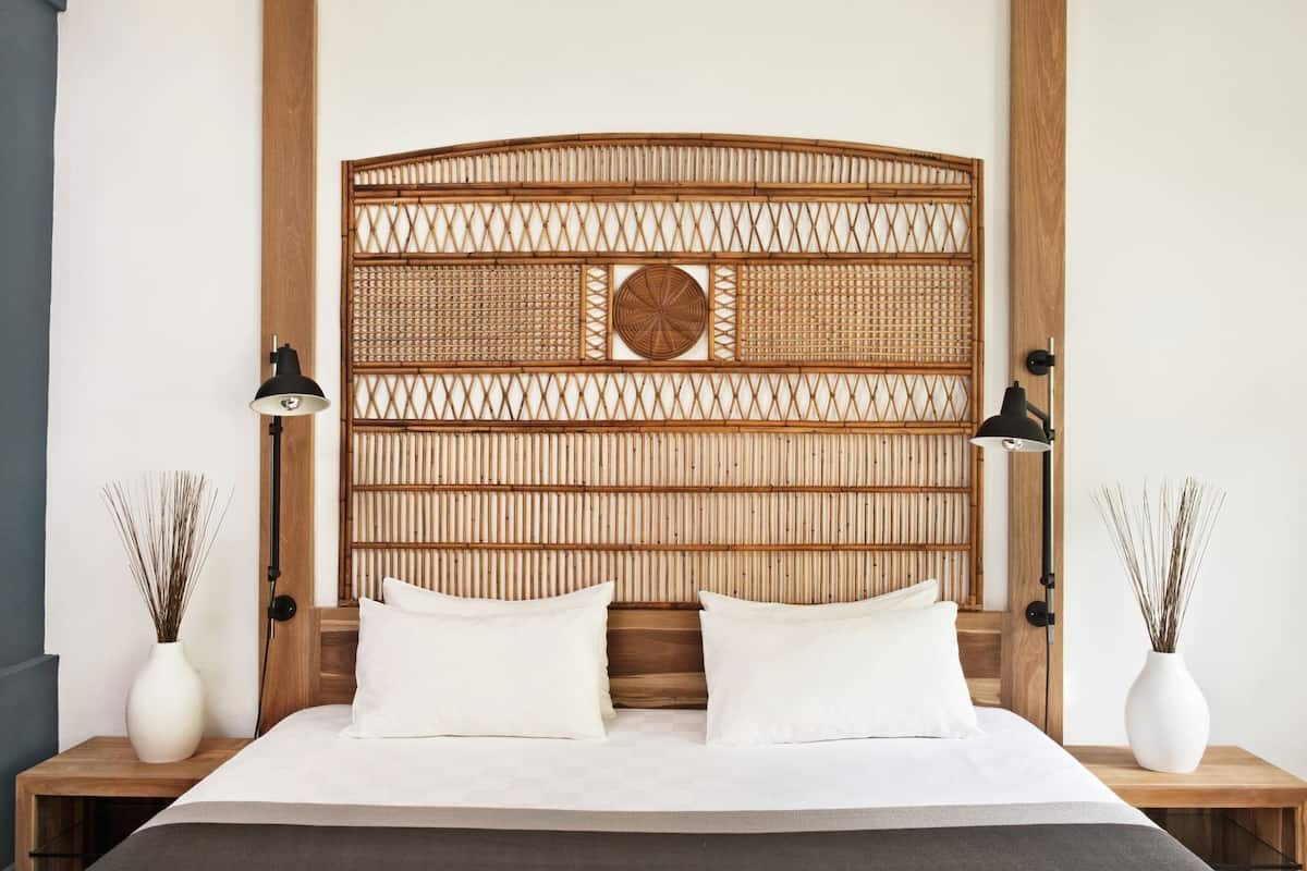 A bed with a woven headboard, two bedside lamps, and two vases of dried plants.