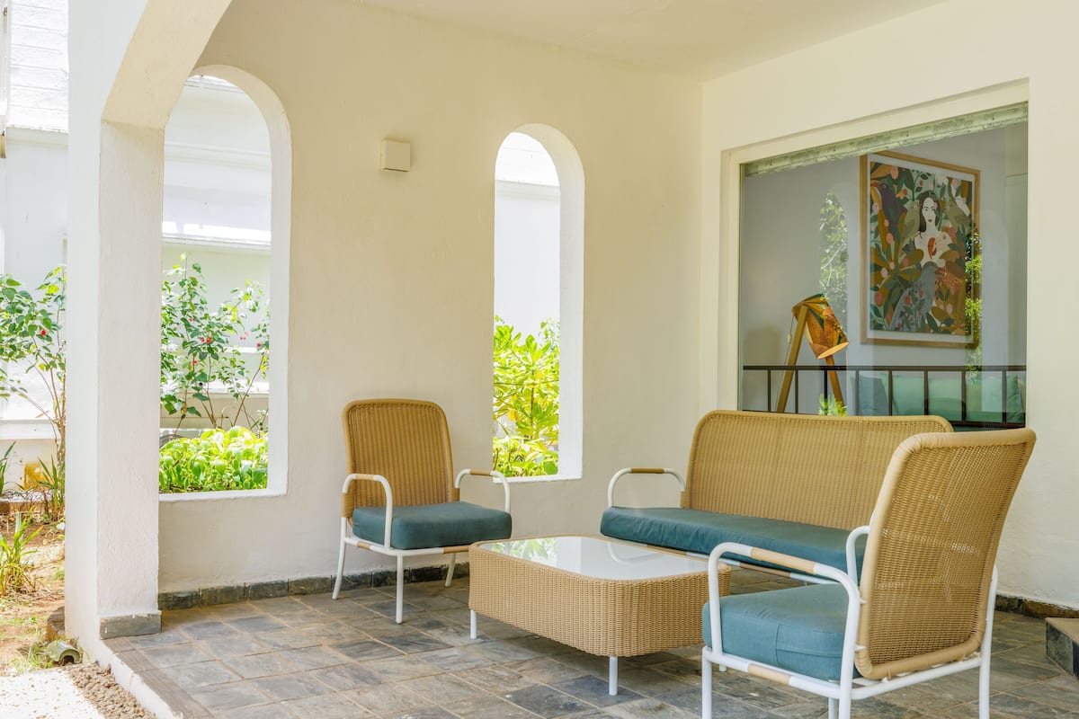 A covered patio with wicker furniture, a glass table, and a painting on the wall.