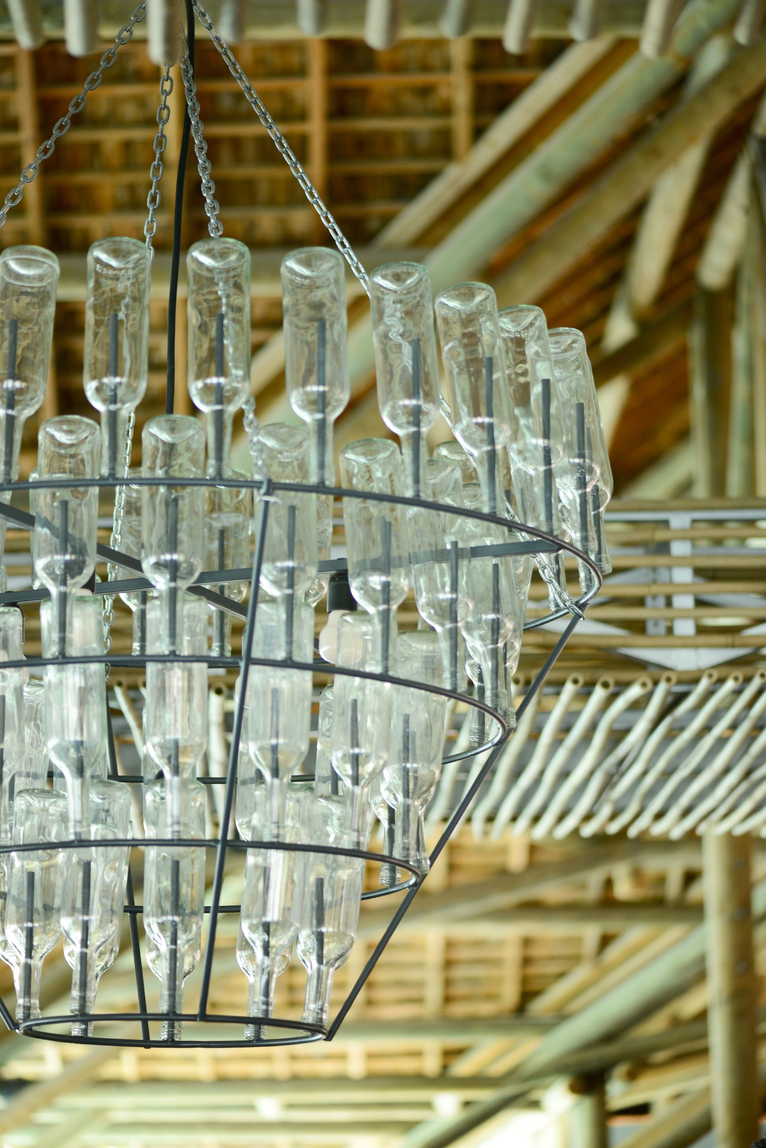 Un candelabro hecho con varias botellas de cristal transparente colgado de una estructura metálica.