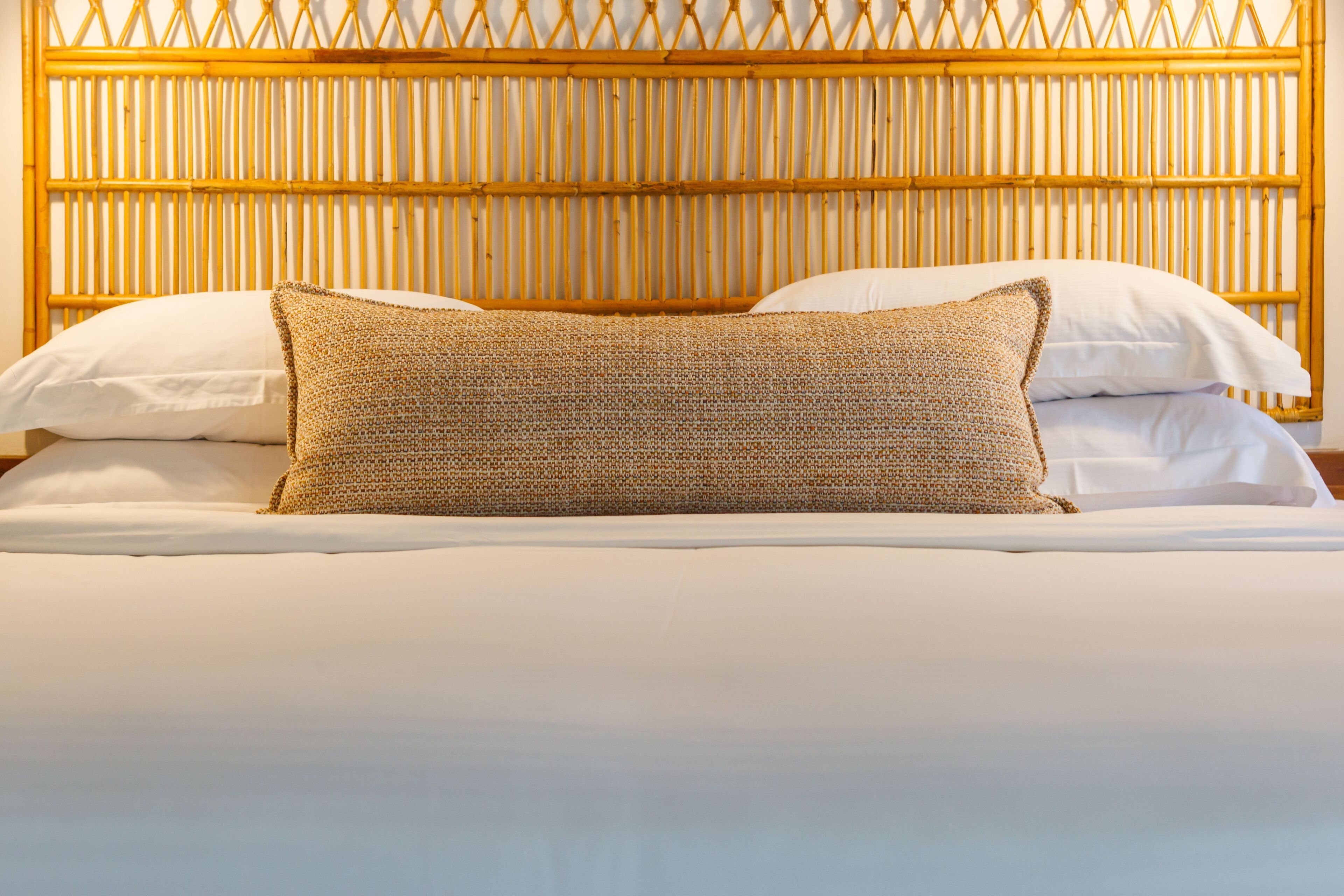 A bed with a woven headboard, white bedding, and a single decorative pillow.