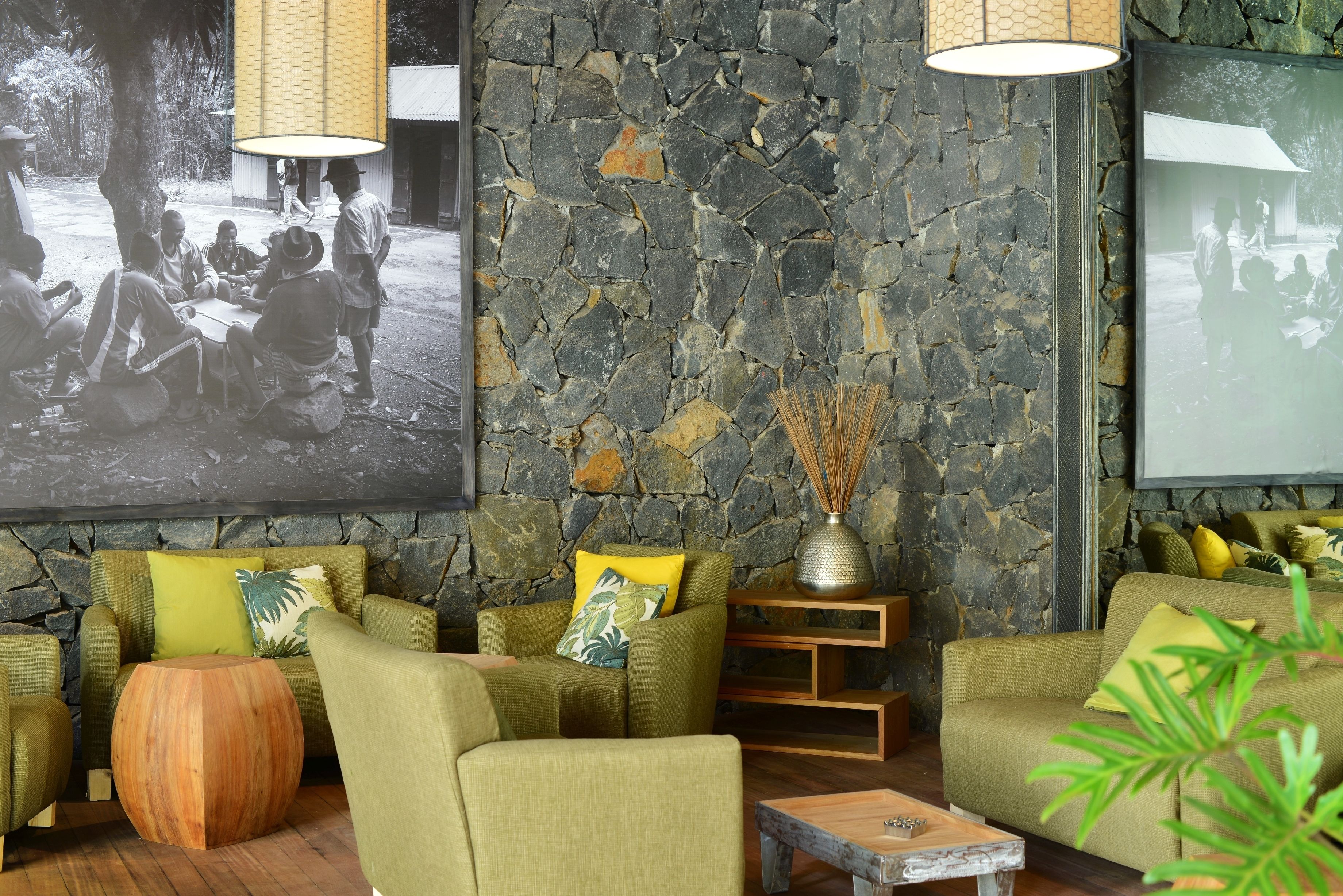 Una habitación con sofás verdes, una mesa de centro redonda de madera y una pared de piedra.