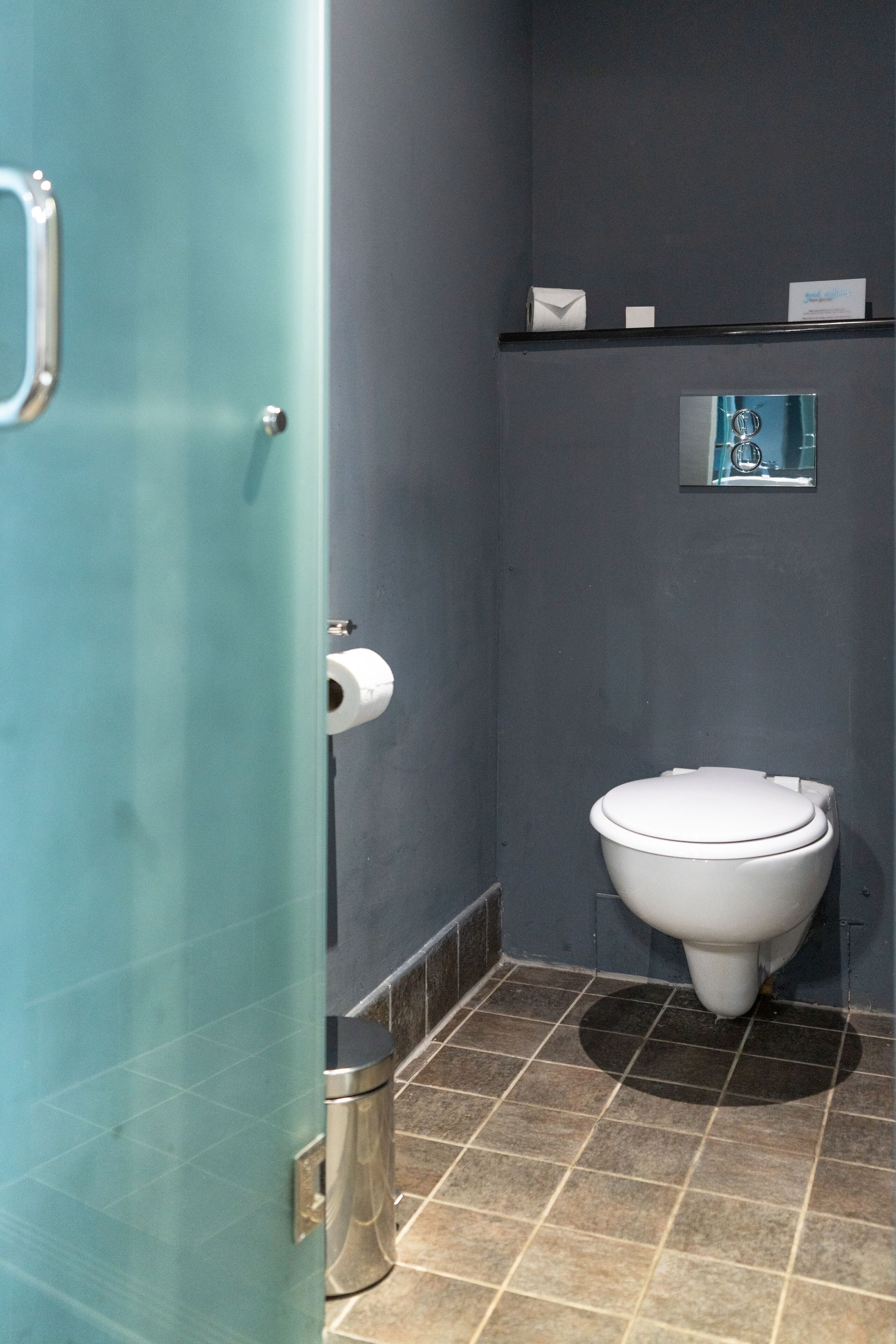 A bathroom with a toilet, a trash can, and a glass door.