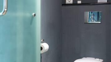 A bathroom with a toilet, a trash can, and a glass door.