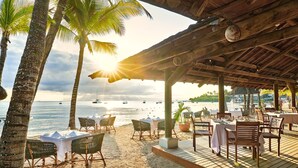 Un restaurante frente al mar con terraza, palmeras y vistas al océano.