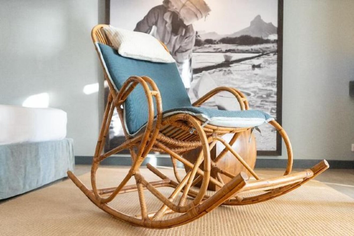 A wicker rocking chair with a cushion, positioned on a woven mat.