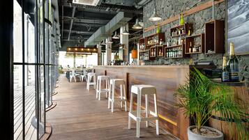 A bar area with wooden flooring, white bar stools, and shelves stocked with bottles.