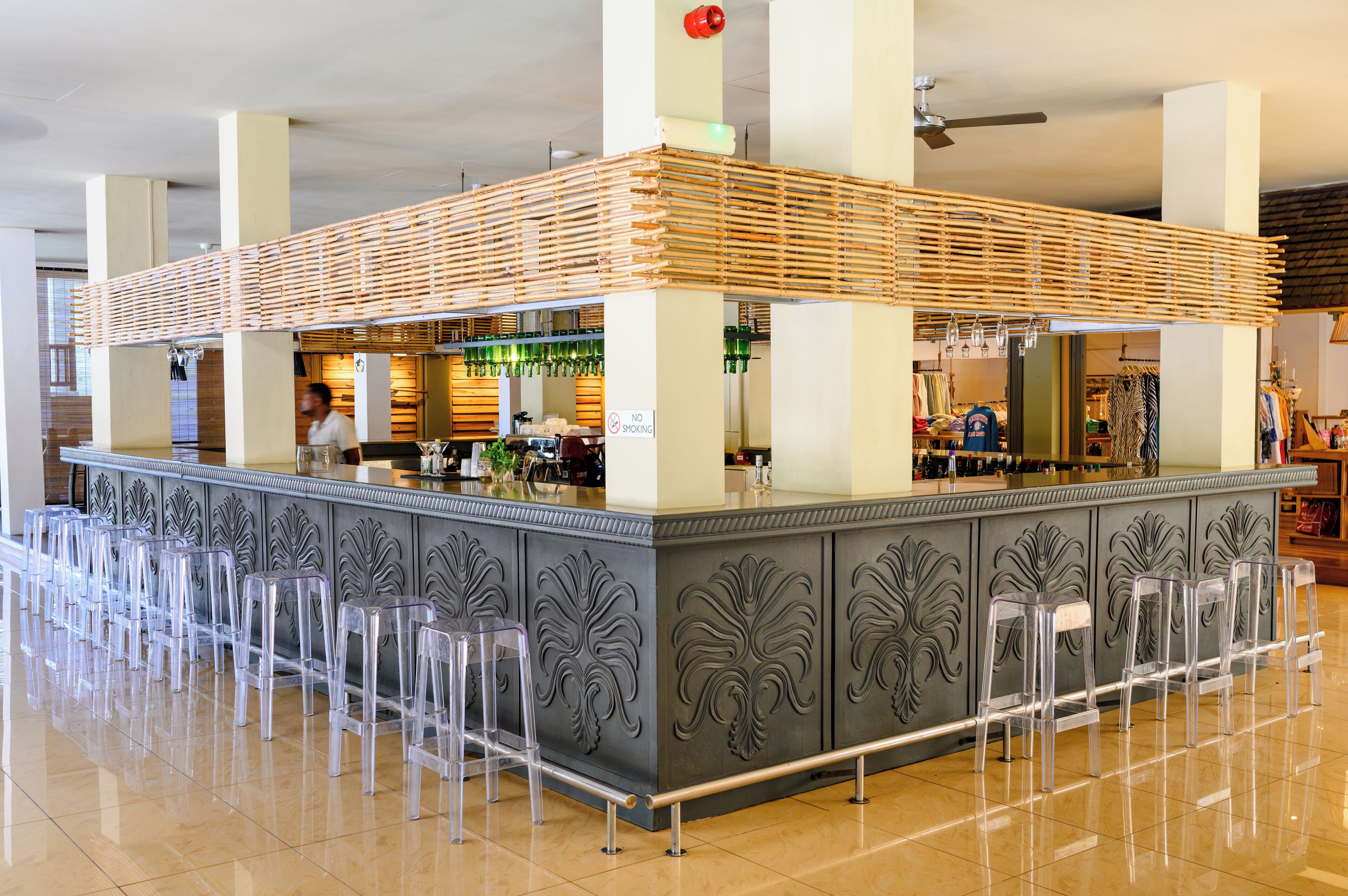 A bar area with a wooden slatted roof, clear plastic stools, and a 'No Smoking' sign.
