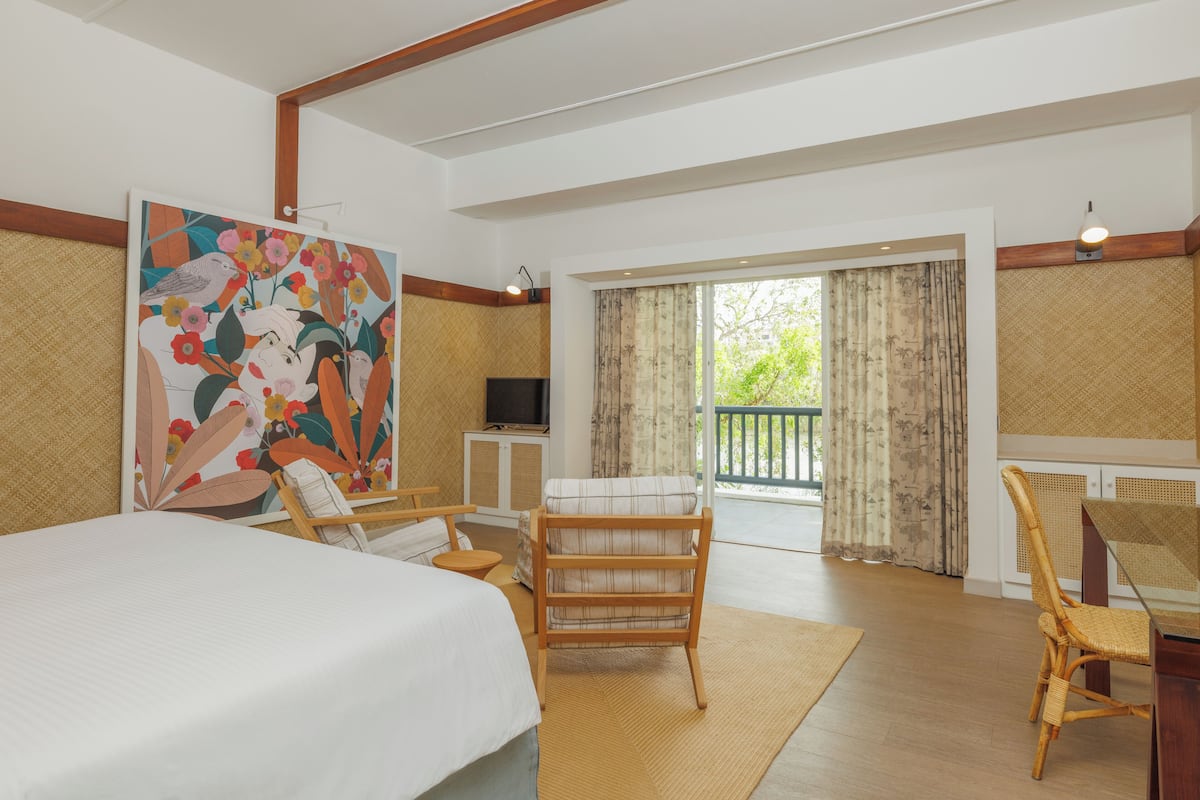 A hotel room with a large bed, a wooden chair, a small table, a television, and a balcony with curtains.