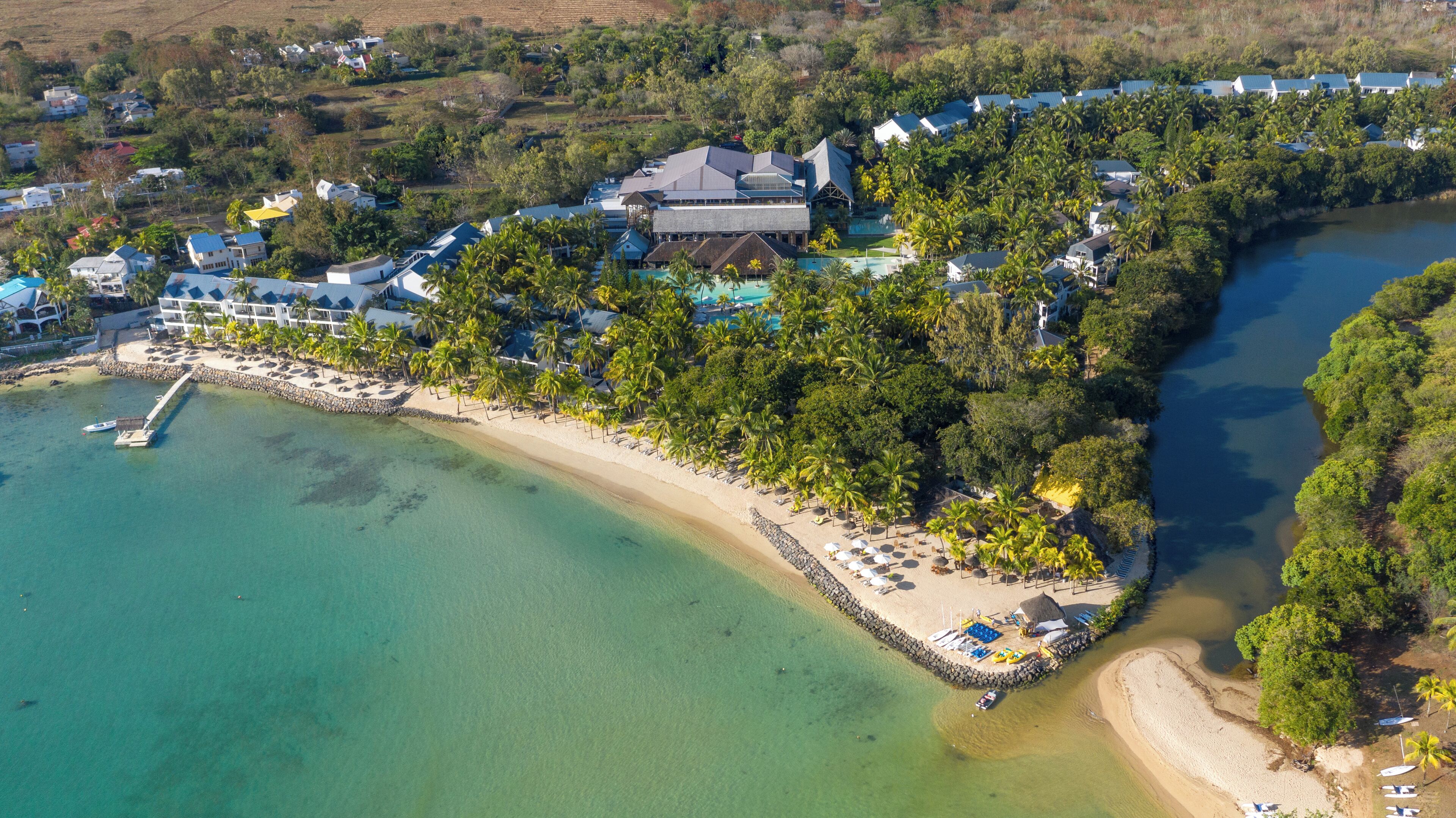 An aerial view of a coastal resort with multiple buildings, a beach, and a clear blue sea.