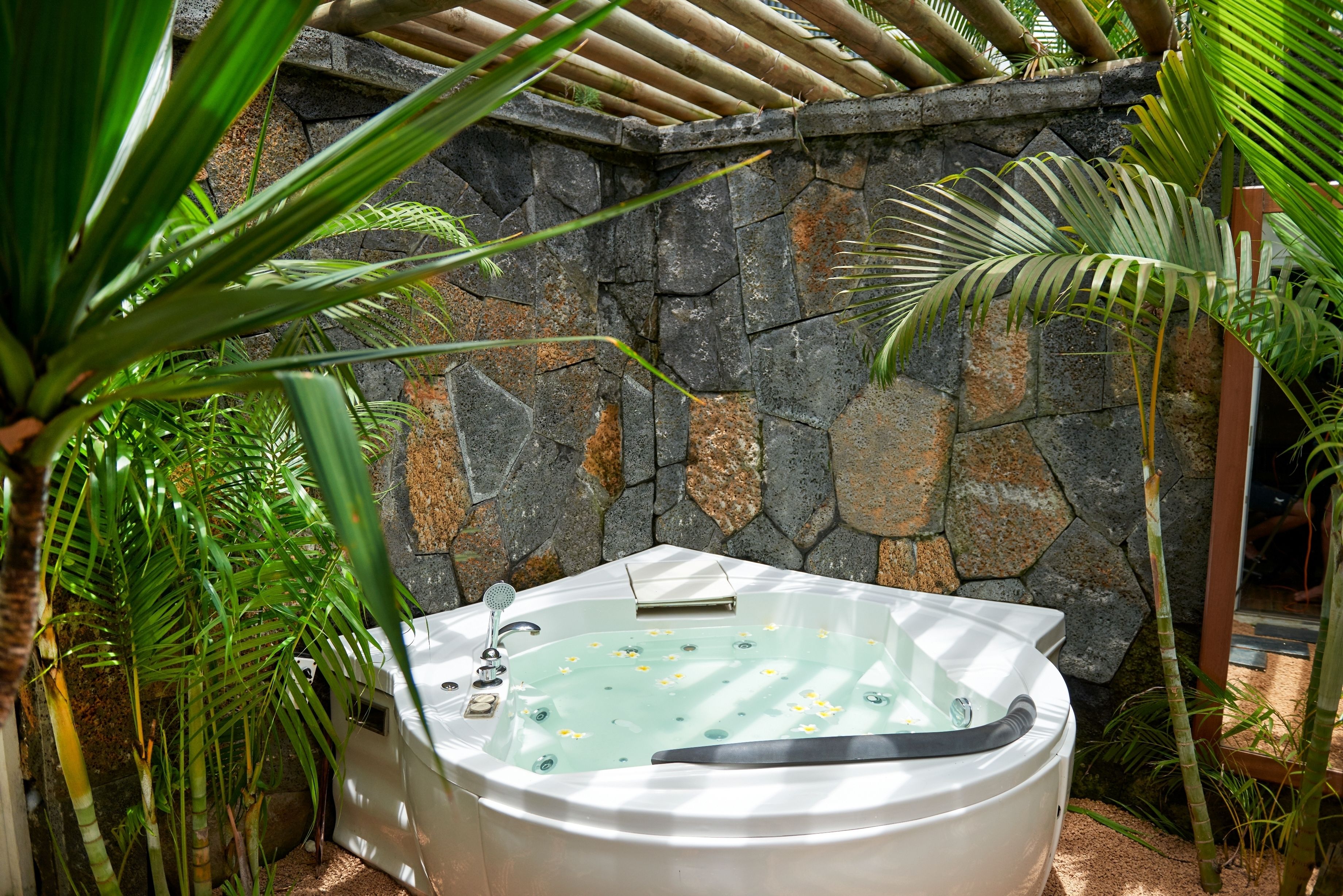 A hot tub surrounded by tropical plants and a stone wall.