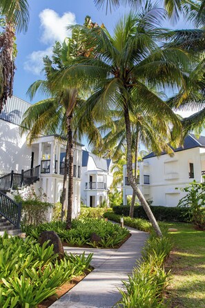 A pathway leading to a white building with balconies, surrounded by lush greenery and palm trees. - The Ravenala Attitude (Balaclava)