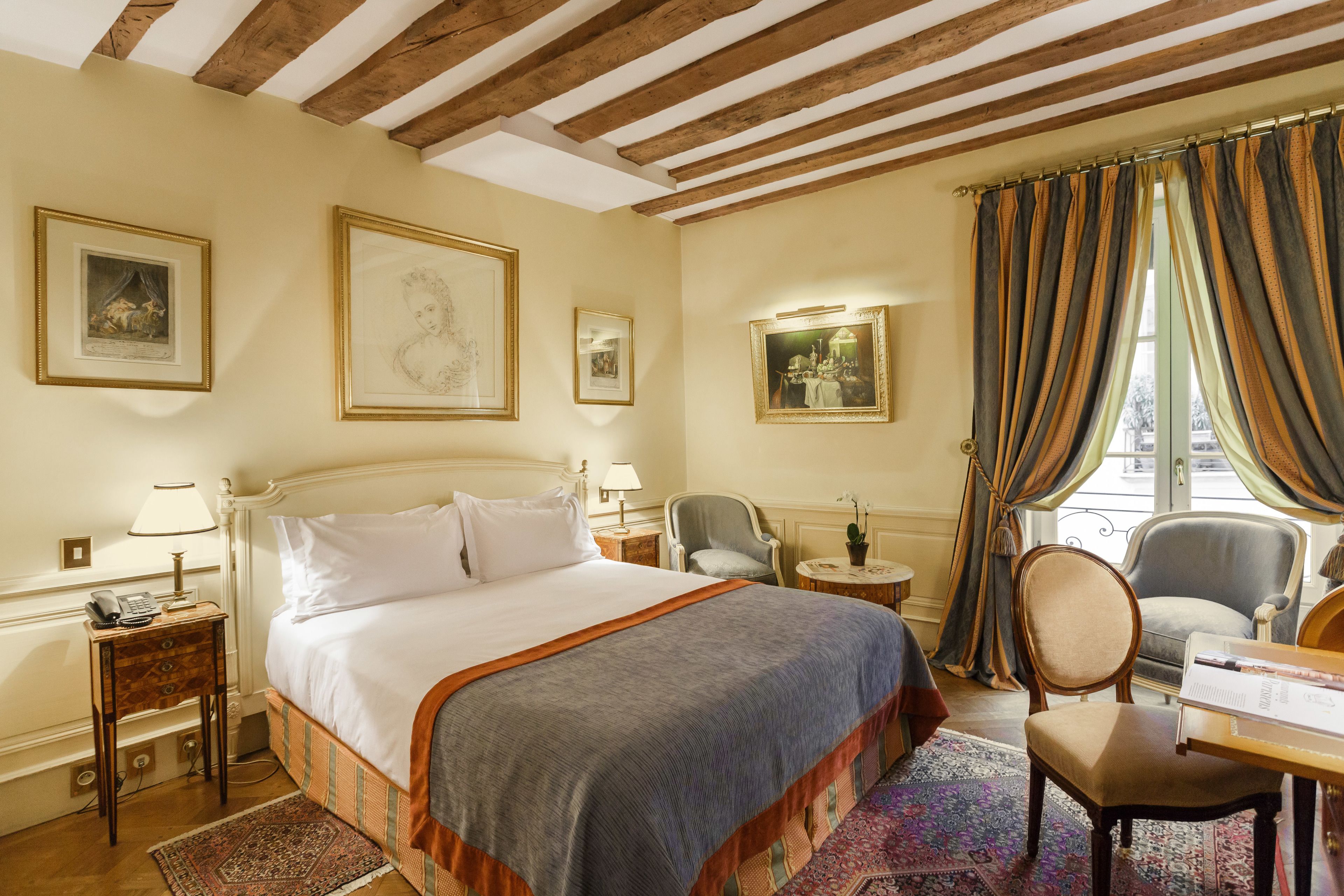 A hotel room with a large bed, a desk, a chair, and a window with curtains.