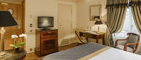 A hotel room with a bed, desk, chair, television, and a potted plant.