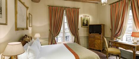 Habitación de hotel con cama, escritorio, silla, televisor y vista a la calle.