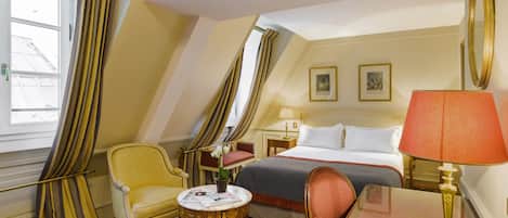 A hotel room with a bed, a chair, a table, and a lamp.