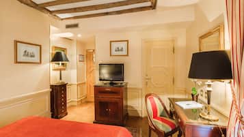 A hotel room with a bed, a desk with a lamp, a television, and framed pictures on the wall.