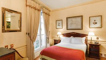 Una habitación de hotel con una cama grande, dos mesitas de noche con lámparas, una silla, un escritorio y un ventanal con cortinas.