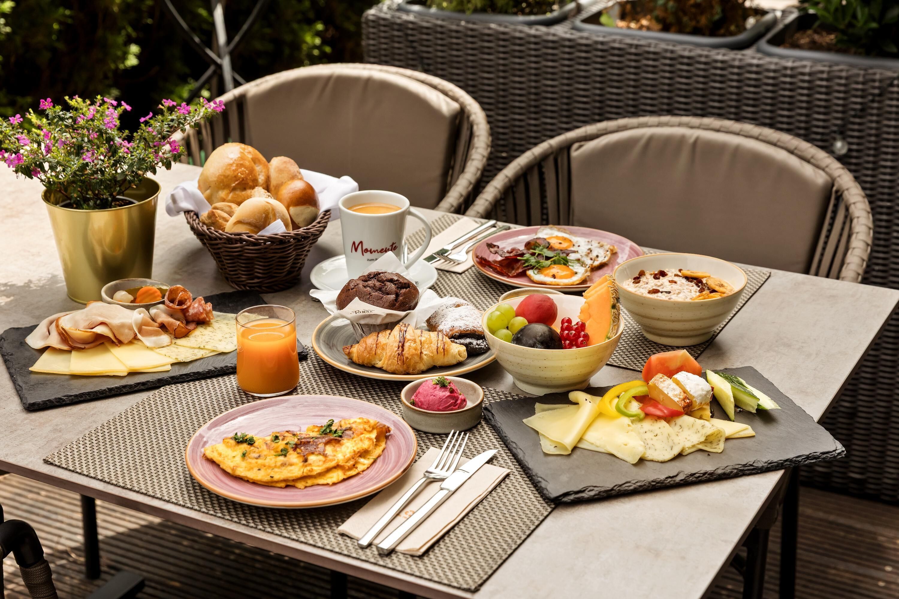 Mesa posta com itens de café da manhã, incluindo ovos, pães e frutas.