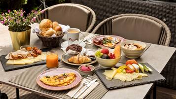 Mesa posta com itens de café da manhã, incluindo ovos, pães e frutas.