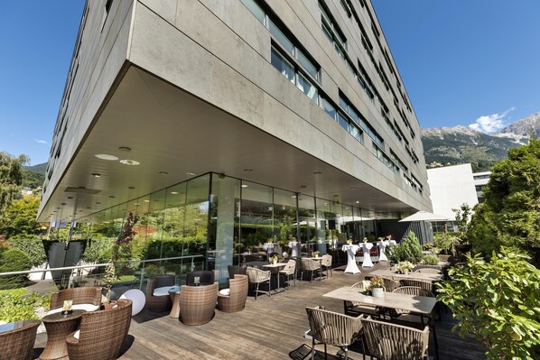 A modern outdoor dining area with wicker furniture and glass walls overlooking a mountainous landscape. - Austria Trend Hotel Congress Innsbruck (Innsbruck)