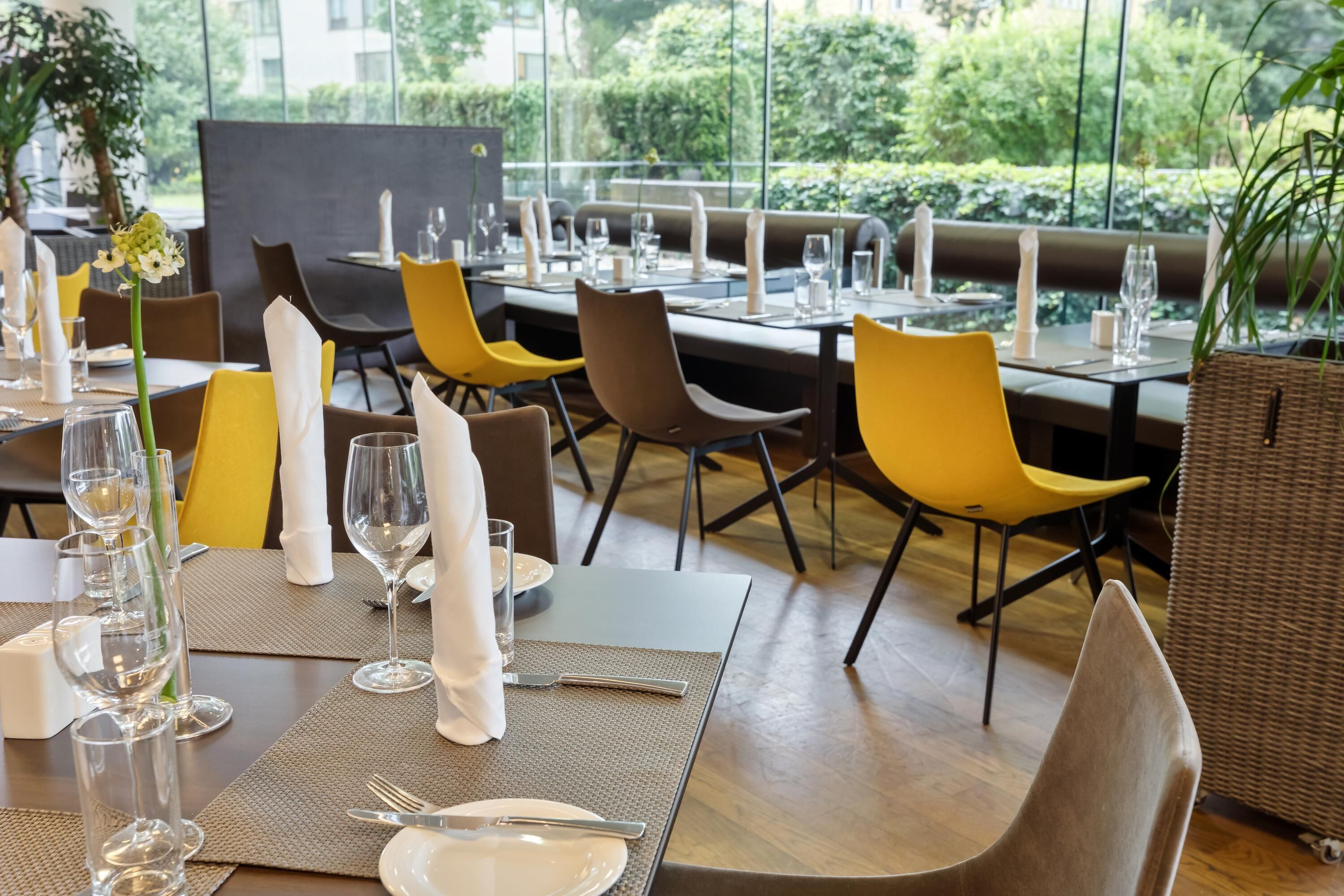 Restaurante con mesas dispuestas para comer, con una combinación de sillas amarillas y marrones, y vistas a zonas verdes al exterior.