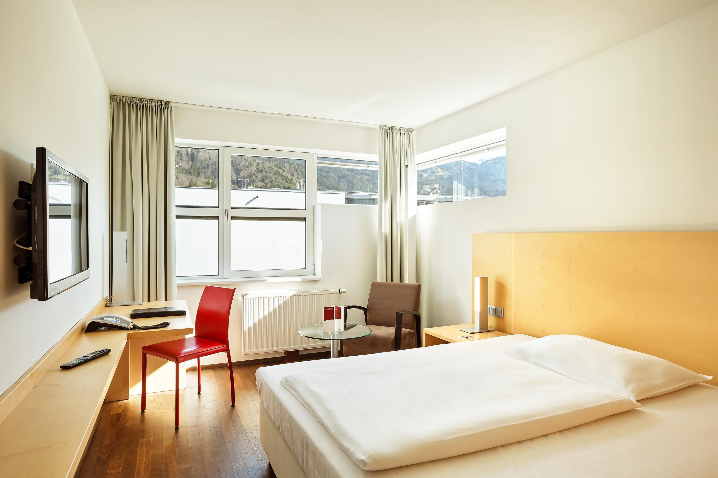 Ein Hotelzimmer mit Bett, Schreibtisch mit Stuhl, Fernseher und einem Fenster mit Vorhängen.