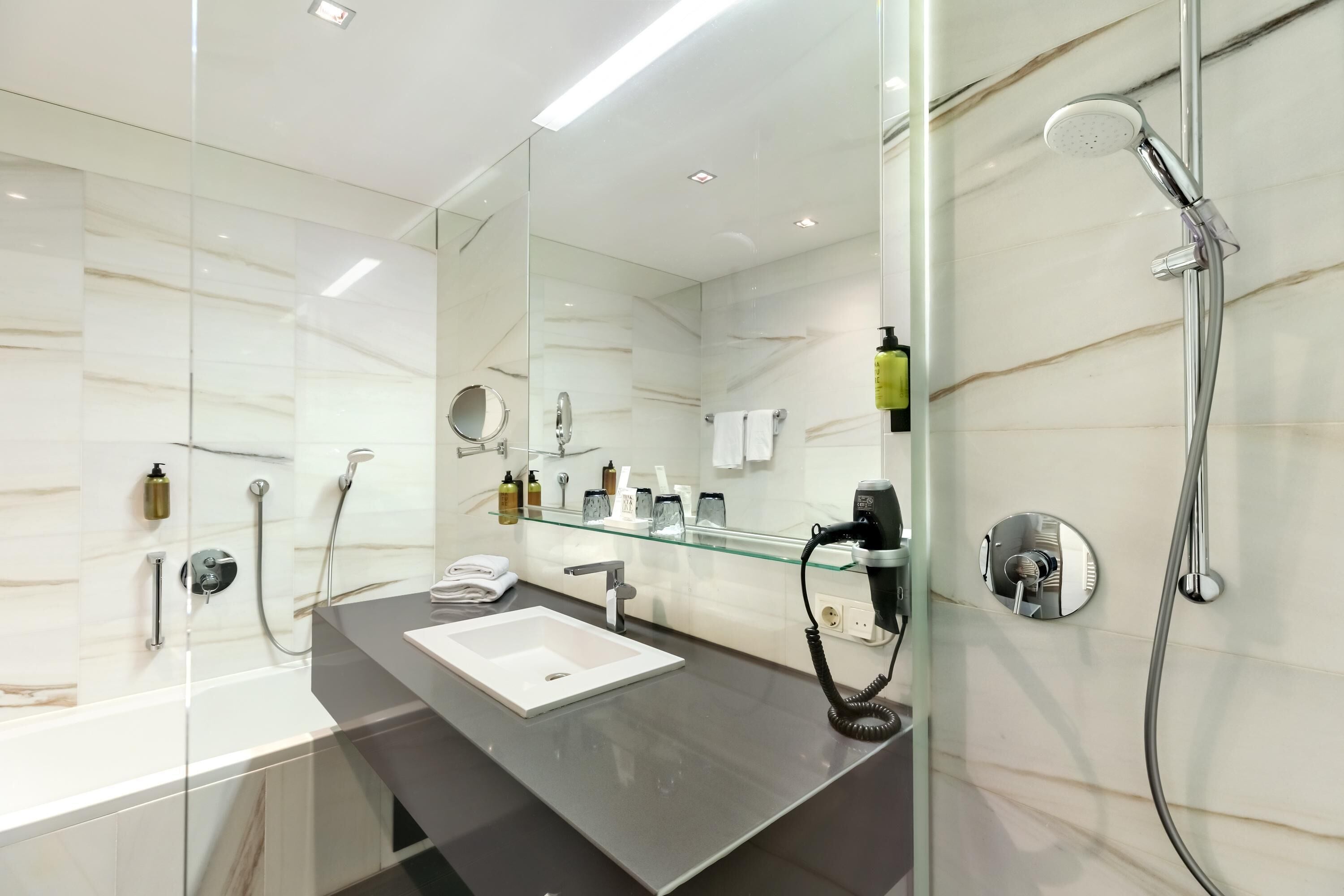 Ein modernes Badezimmer mit Duschkabine aus Glas, einem weißen Waschbecken und einer Glasablage für Toilettenartikel.