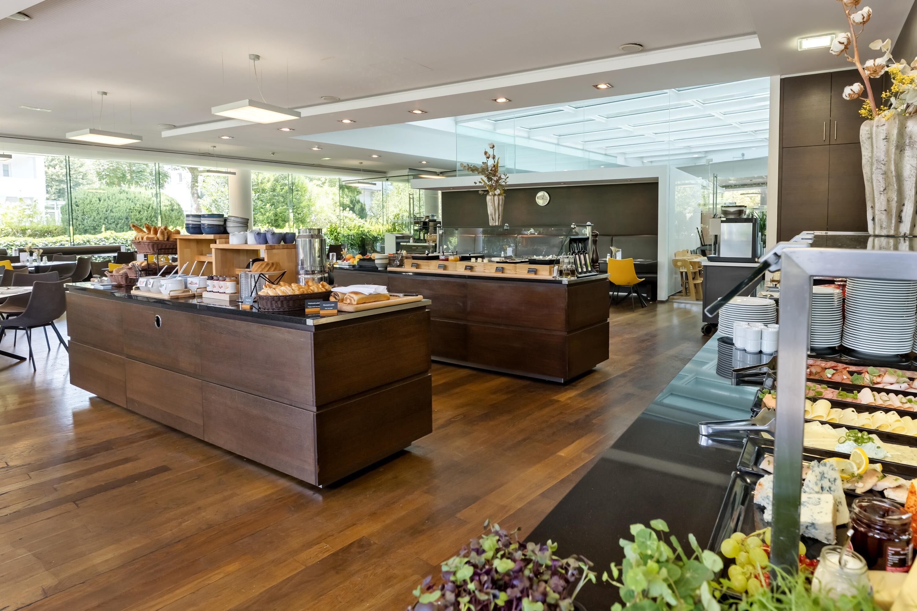 Ein moderner Essbereich mit Holztischen, einem Buffet und Blick ins Freie.