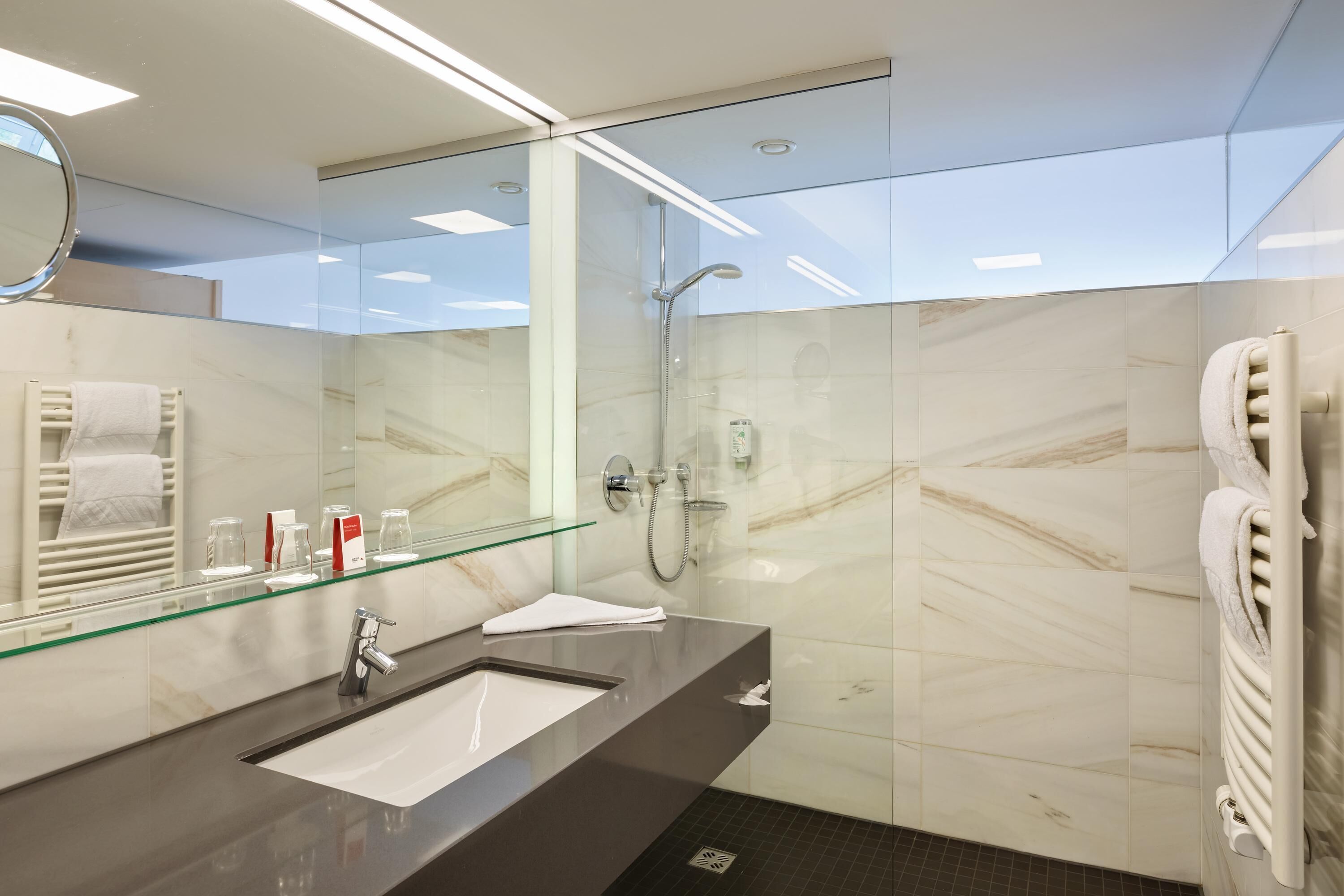 Un baño moderno con cabina de ducha de vidrio, encimera oscura, espejo y perchero.
