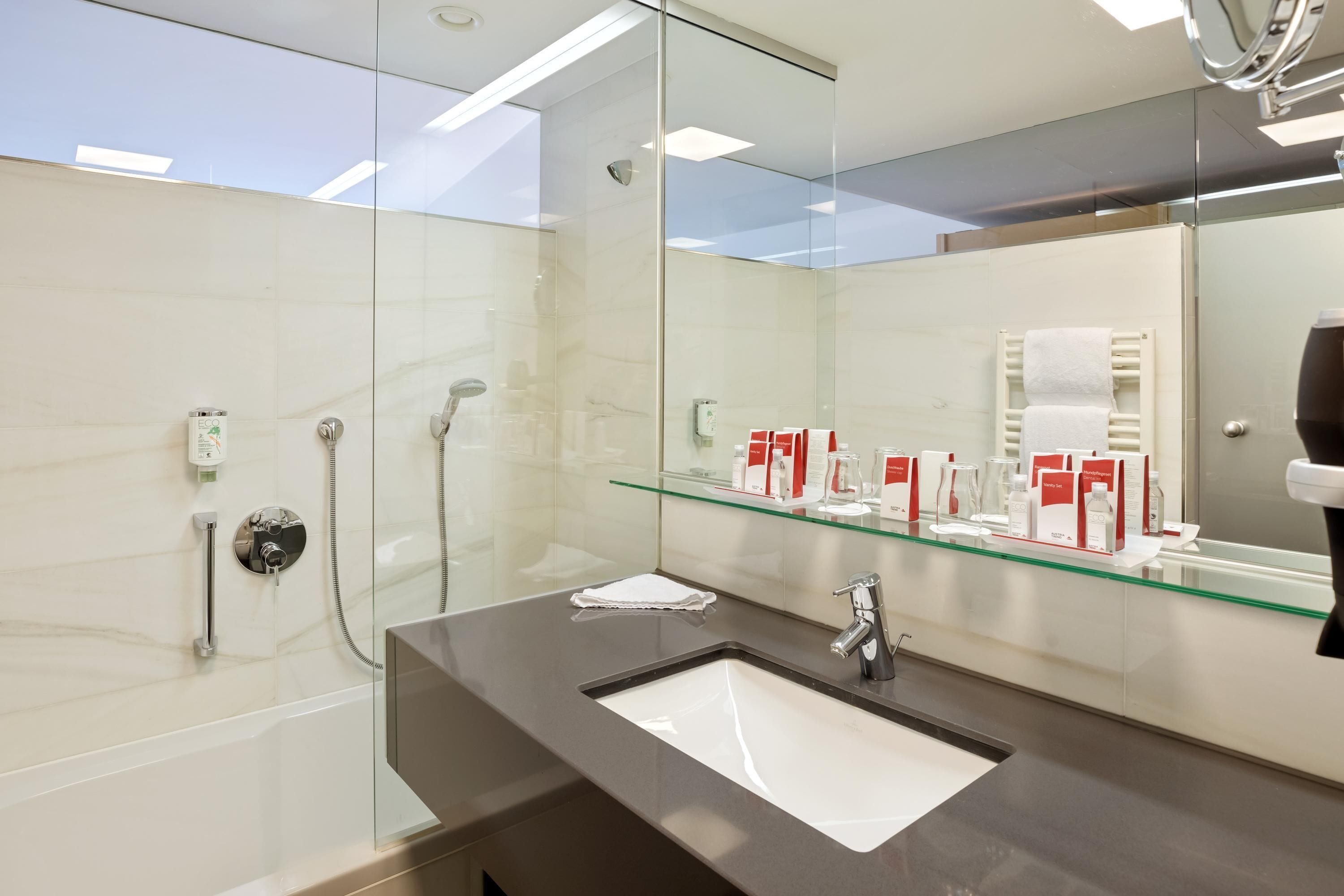 A modern bathroom with a glass shower enclosure, a sink with a mirror, and a glass shelf with toiletries.