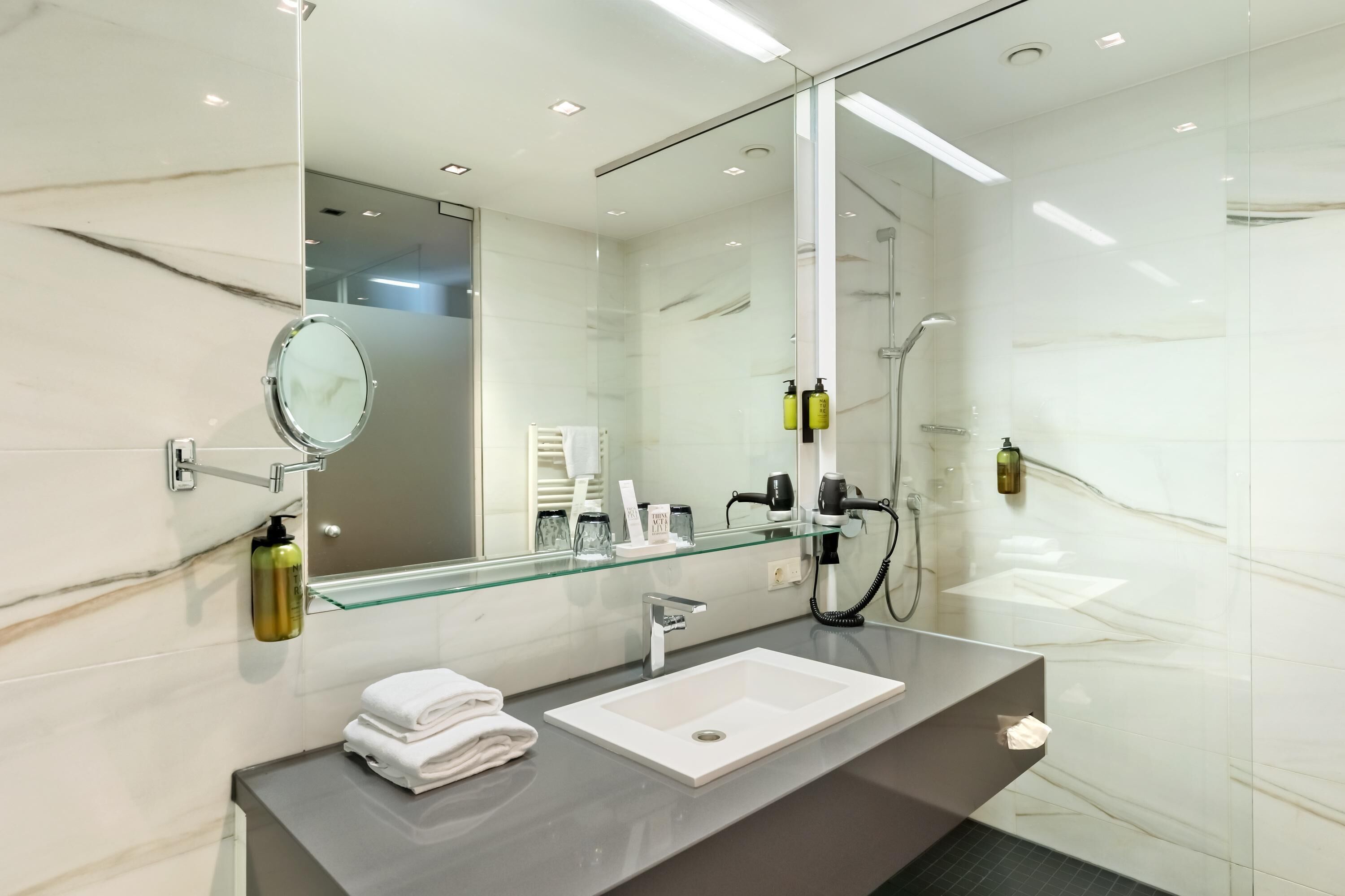 Un baño moderno con pared de azulejos de mármol, cabina de ducha de cristal, lavamanos blanco y un espejo grande.