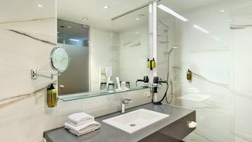 Un baño moderno con pared de azulejos de mármol, cabina de ducha de cristal, lavamanos blanco y un espejo grande.