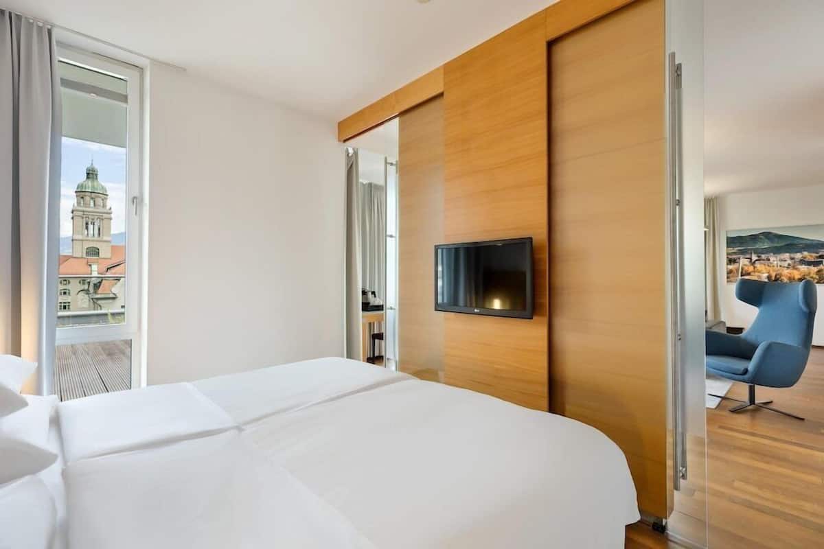 Camera d'albergo con un letto grande, una televisione a schermo piatto montata a parete e vista sulla città attraverso una porta vetrata.