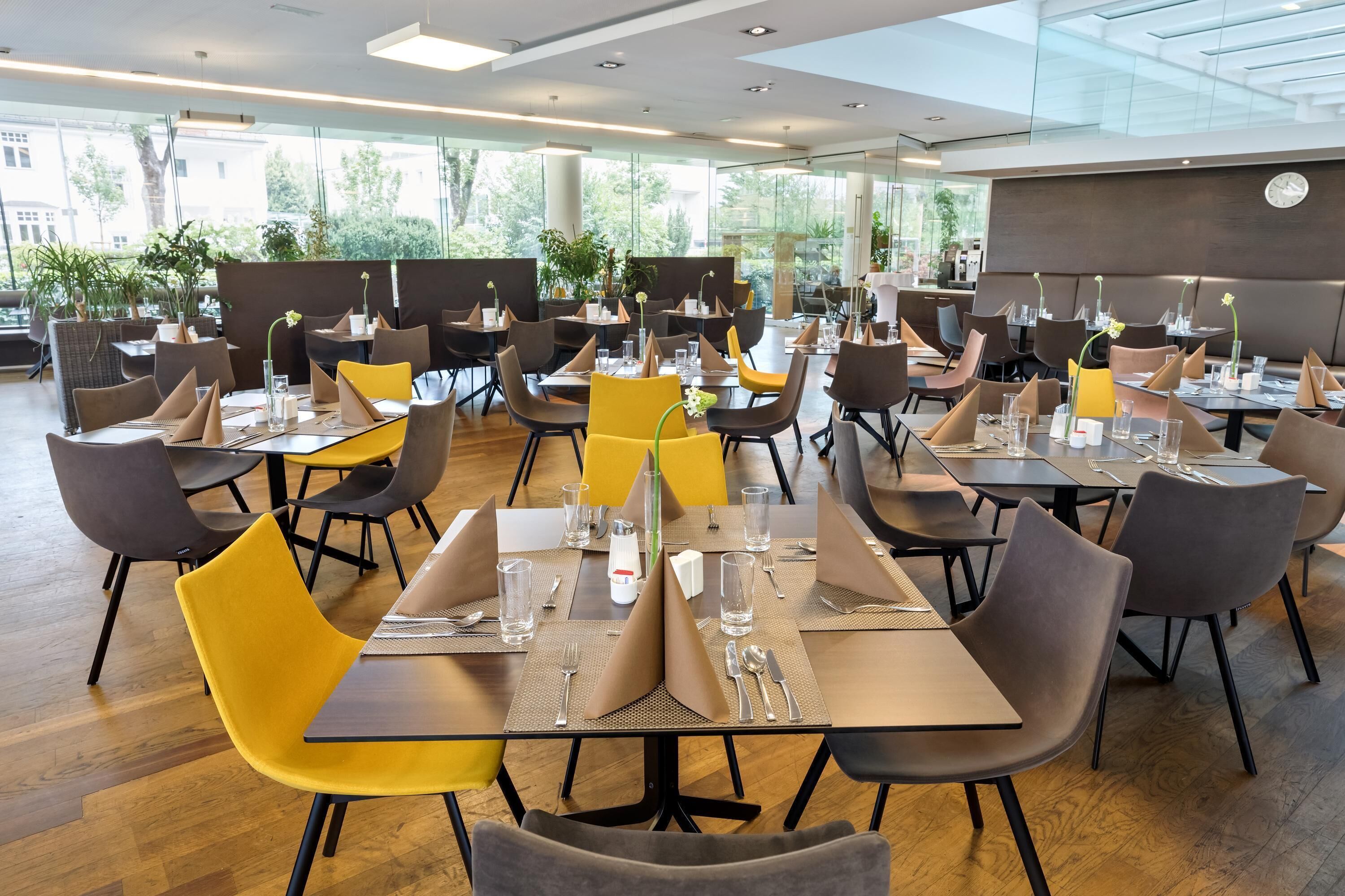 A modern restaurant with multiple tables and chairs, arranged in a spacious layout with large windows offering views of the outdoors.