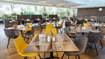 A modern restaurant with multiple tables and chairs, arranged in a spacious layout with large windows offering views of the outdoors.