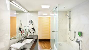 A modern bathroom with a glass shower enclosure, a large mirror, a vanity with a sink, and a towel stacked on the floor.