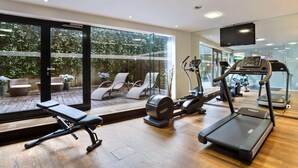 Una palestra moderna con tapis roulant, ellittica e panca pesi. Ampie finestre offrono vista su posti a sedere all'aperto e aree verdi.