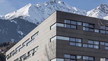 A modern building with a flat roof and multiple windows, set against a backdrop of snow-capped mountains.