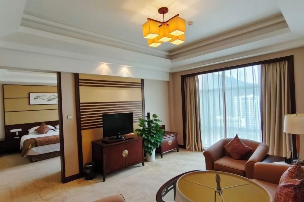 A hotel room with a bed, a television, a sofa, a coffee table, and a large window with curtains.