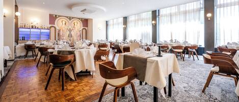 A spacious dining area with multiple tables and chairs, large windows, and a decorative wall.