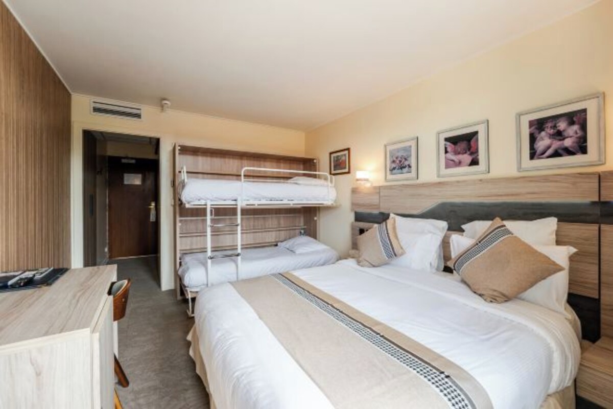 Een hotelkamer met een stapelbed, een bureau en een bed met kussens en dekbed.