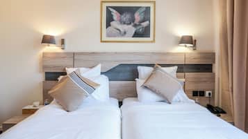 Une chambre d’hôtel avec deux lits, une tête de lit en bois, des lampes de chevet, un tableau encadré au mur et un téléphone sur la table de chevet.