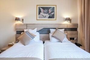 Ein Hotelzimmer mit zwei Betten, einem Holzkopfende, Nachttischlampen, einem gerahmten Bild an der Wand und einem Telefon auf dem Nachttisch.