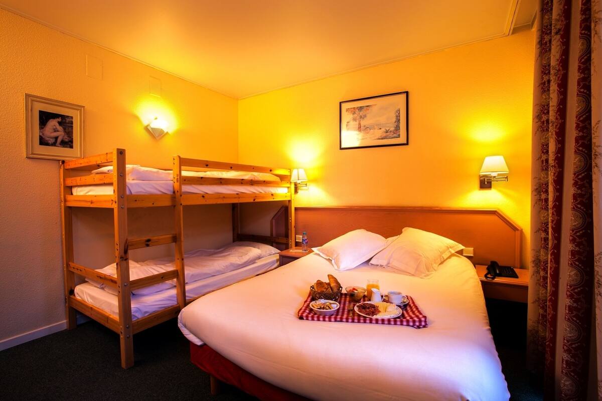 A hotel room with two bunk beds, a bedside table with a lamp, a framed picture on the wall, and a breakfast tray on the lower bunk bed.