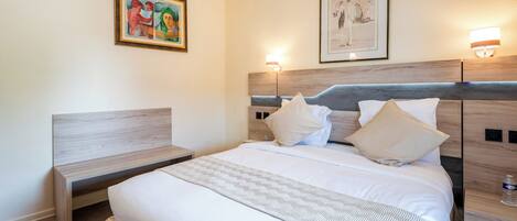 A hotel room with a bed, bedside tables, a bench, and two wall-mounted lamps.