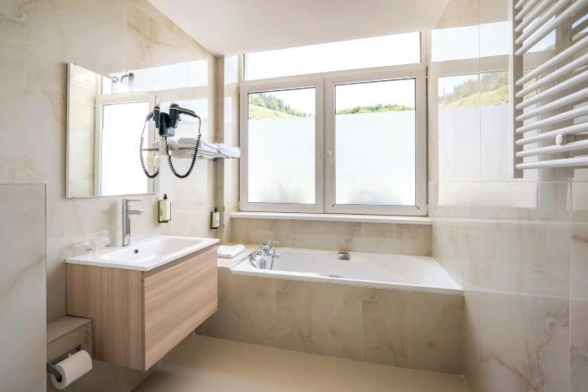 Een moderne badkamer met een groot raam, een badkuip en een wastafel met spiegel.