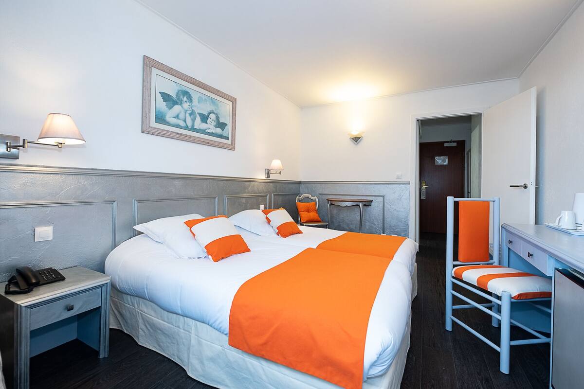 A hotel room with a bed, bedside table, lamp, and a desk with a chair.