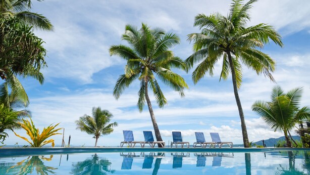 A clear blue pool with four lounge chairs and palm trees.