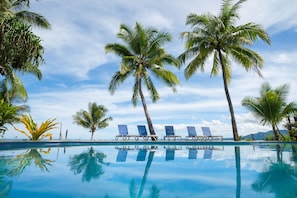 A clear blue pool with four lounge chairs and palm trees.